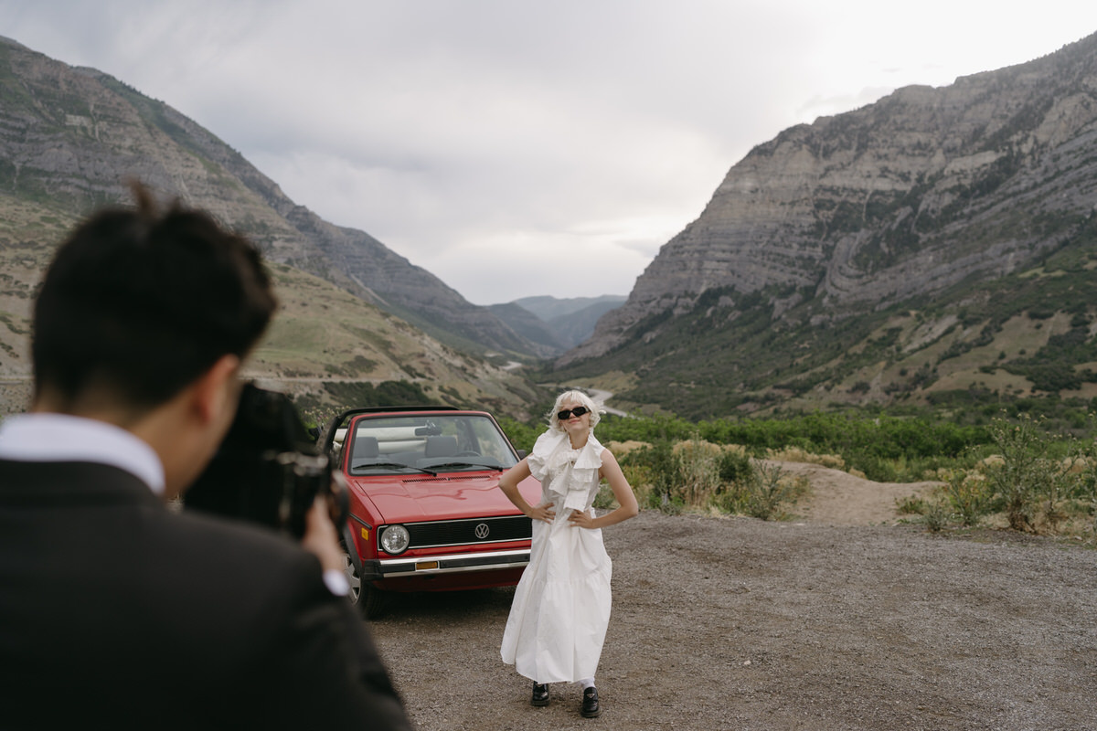 groom taking film photograph of his bride in font of red volkswagen convertible